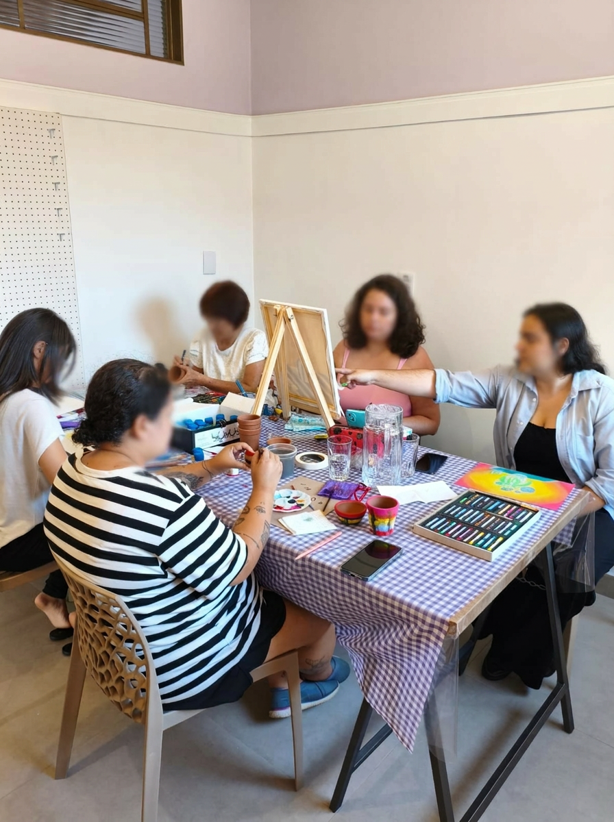 Mulheres reunidas em mesa criativa com materiais artesanais coloridos, rindo e criando juntas