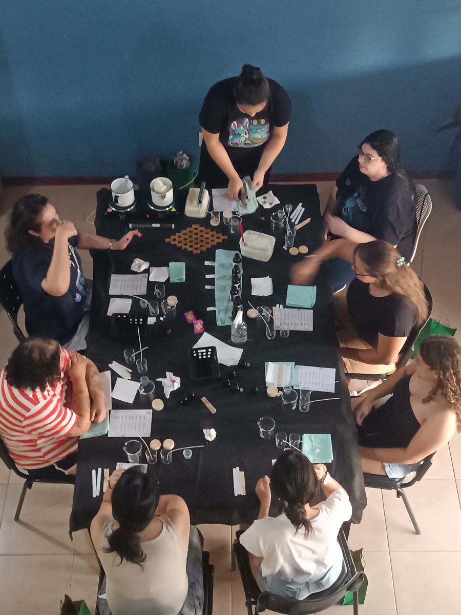 Vista de cima da mesa da oficina Essência com as participantes produzindo velas perfumadas