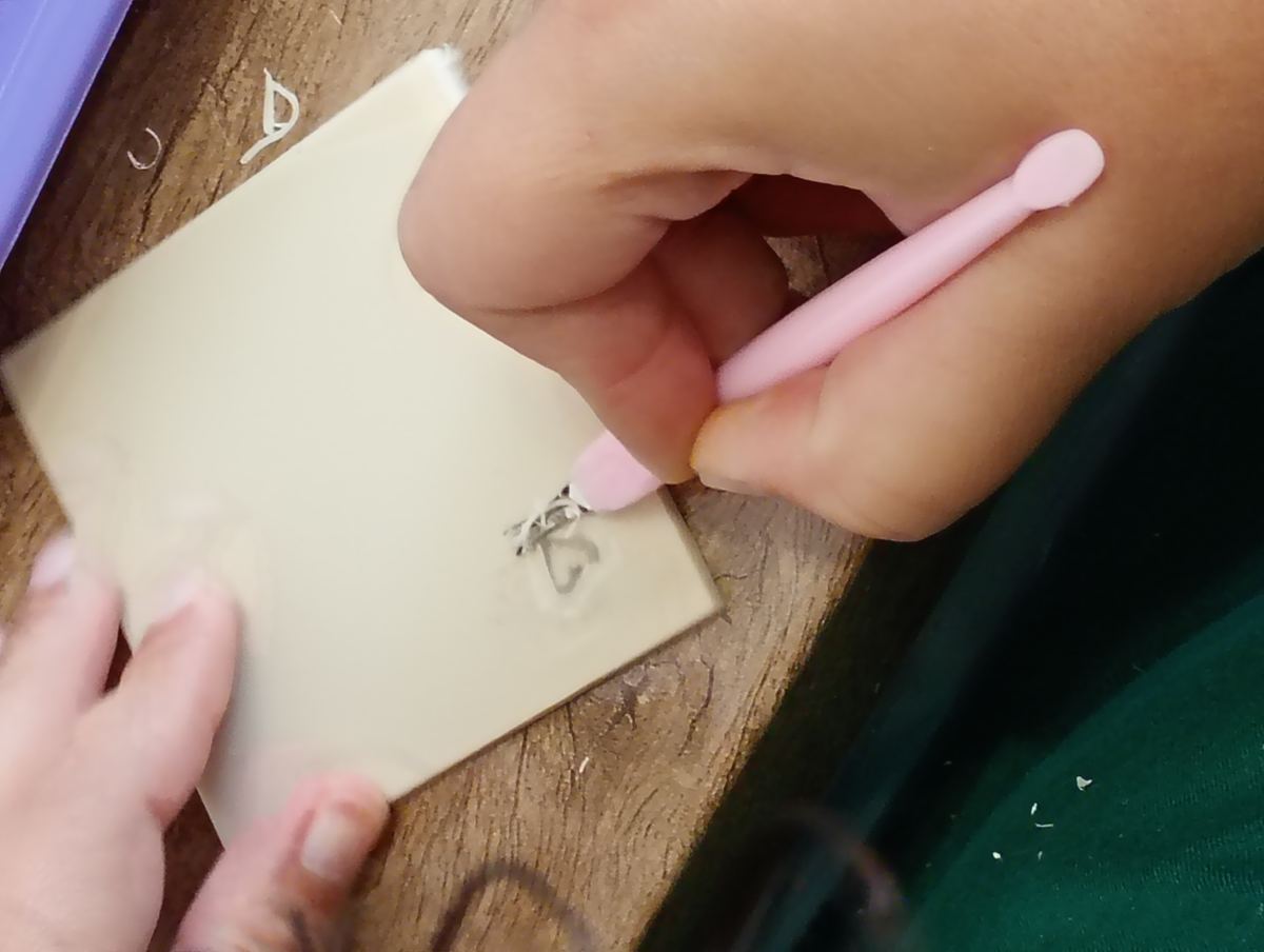 Mãos de participante entalhando um carimbo artesanal na oficina Impressões