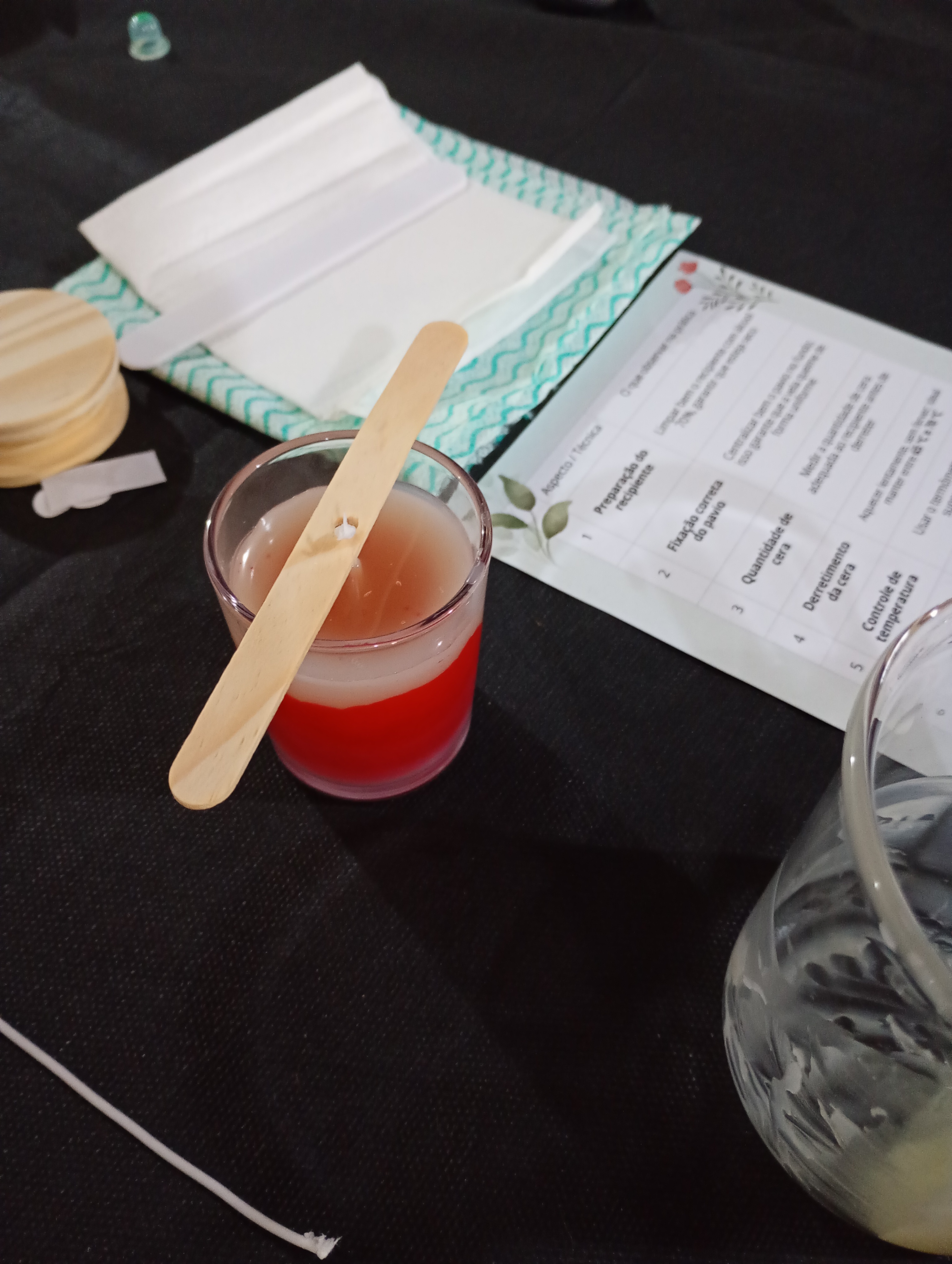 Mulher sorridente mostrando orgulhosa sua primeira peça de crochê finalizada na oficina, enquanto outras participantes aplaudem ao redor da mesa